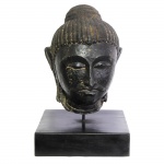 Importante cabeça de Buda executada em pedra,com pintura monocromática na cor negra. Acompanha base em madeira. Índia, Séc. XIII. 37 cm sema base e 48 cm com a base.