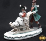 Bibelot em porcelana alemã de dama no trenó sendo empurrada por um cavalheiro. Medindo a escultura 16,5cm de largura x 14cm de altura. A pás da frente do trenó estão faltando.