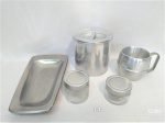 Lote de cozinha 5 peças em metal prateado. Sendo 1 caneca em aluminio com 11cm de altura; 01 centro de mesa em aço inox Wolff com 31x17cm de comprimento; 02 potes em vidro com tampa em aluminio com 5 e 7cm de altura e 01 pote de aluminio, marca rochedo, com 14cm de altura.