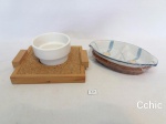 Lote 2 petisqueiras em porcelana decoradas, uma com base em madeira e uma com base em palha.Medida: Redonda: 10cm de diametro e a Oval: 18cm.