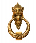 Batedor de porta em metal amarelo fundido e polido. Representado por figura leonina embocada à coroa de elementos vegetais. Século XX. 22 x 13 x 6 cm.