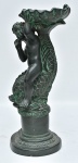 Grande castiçal confeccionado em estuque patinado, imitando bronze, representando "putino sobre tritão", repousados sobre pedestal. Med.: 42x17 cm. Obs.: Apresenta pequenos bicados.