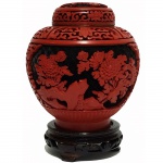 Vaso em laca com tampa nas cores preta e vermelha com decoração em relevo de vegetação e base em madeira. China, Séc. XX. 14 cm sem a base e 17 cm com a base.