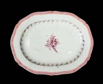 CIA DAS INDIAS  ELEGANTE TRAVESSA EM PORCELANA CIA DAS INDIAS (FORMA PAR IDENTICO COM A OFERTADA NO LOTE ANTEIROR) COM ESMALTES DA FAMILIA ROSA. REINADO QIANLONG (1711  1799). BORDA RECORTADA, DECORADA COM GREGA NA TONALIDADE ROSE DELIMITADA POR FILETES ROUGE DE FEUR. TRANSIÇÃO DA BORDA PARA A CALDEIRA COM GUIRLANDA EM AZUL COM PARRAS E CACHOS DE UVA. NA CALDEIRA RESERVA CONTENDO RAMALHETE FLORAL. FUNDO TEM CERÂMICA APARENTE. CHINA, SEC. XVIII. 27 CM DE COMPRIMENTO