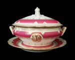 CORONEL JOÃO PINTO DA FONSECA GUIMARÃES. BELA TERRINA E SEU PRESENTOIR   EM PORCELANA  COM BORDA DECORADA EM ROSE POMPADOUR REMATADA FOR FINO OURO EM GUIRLANDAS. RESERVAS COM INICIAIS ENTRELAÇADA JP. TAMPA COM FEITIO CAMPANULAR. PERTENCEU AO SERVIÇO DO CORONEL JOÃO PINTO DA FONSECA GUIMARÃES. FRANÇA, MEADOS DO SEC. XIX. 24 CM DE DIAMETRO.