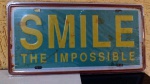 Placa em formato automotivo temática "SMILE - THE IMPOSSIBLE", impressão no metal com cantos arredondados e furos para fixação (4) - importada medindo 15,5 X 30,5 centímetros, NOVA na embalagem / sem uso -
