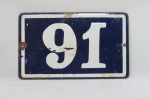 Placa esmaltada com o número 91, a qual era fixada nas antigas residências