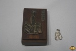 Lote de caixa de música em madeira e 1 pingente em metal prateado, ambos com a imagem de Nossa Senhora de Fátima. Medindo a caixa 9cm de altura.