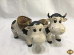 Par de vacas em cerâmica pintada com cesto floreira. Medindo a que está de pé 22,5cm de comprimento x 15cm de altura.