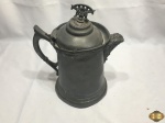 Grande leiteira antiga em estanho trabalhado. Medindo 25,5cm de altura. A tampa está solta e a peça possui algumas perdas na borda.