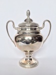 Ânfora em metal banhado à prata, anos 60. Base circular, bojo liso e abaulado com faixas estilizadas. Alças recurvas e tampa com pega no formato de pinha.  Manufatura EBERLE gravado embaixo do exemplar. Dimensões: 18 cm altura x 15 cm largura.