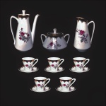 SCHMIDT - Conjunto tete-a -tete em porcelana esmaltada, anos 60,  decorado com flores, faixa bordô e frisos gravados à Ouro 22 k.Total de 7 peças. Bule, açucareiro, leiteira, 02 xícaras para café e 02 pires. Exemplares antigos e em perfeito estado de conservação.