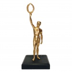 Estatueta em metal com pátina dourada representando " Homem Grego Romano com coroa de louros", sobre base em mármore preto. Presença de duas équenas perfurações na base. Dimensões: 24 cm x 10 cm x 10 cm.