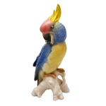 Estatueta de porcelana alemã policromada representando catatua empoleirada em galho, predominando as cores azul e amarela. No verso marcas da manufatura e as inscrições: ENS  Germany.  (KARL ENS. 1919 / 1940). 19 cm.
