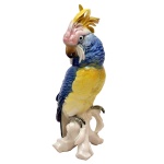 Estatueta de porcelana alemã policromada representando catatua empoleirada em galho, predominando as cores azul e amarela. No verso marcas da manufatura e as inscrições: ENS. (KARL ENS. 1919 / 1940). 28 cm.
