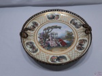 Fruteira centro de mesa em porcelana com cena galante e acabamento em metal dourado. Medindo 31,5cm de diâmetro x 12,5cm de altura.