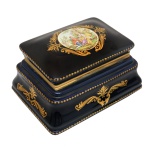 Caixa retangular em porcelana de cor azul noturno, realçada por estilizações douradas e adornos em bronze. Tampa com decoração de cena romântica entre grande reserva em ouro. No fundo as inscrições: Modelo Mignon Decoré & Limoges à la Main. Séc. XX. 14 x 23 x 17 cm.