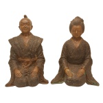 Par de esculturas japonesas em bronze representando casal de dignitários ajoelhados, vestindo trajes formais. Séc. XIX. 29 x 17 x 17 cm / 28 x 20 x 15 cm.