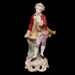 Estatueta em porcelana alemã policromada representando menino em trajes formais. Base recortada e vazada. No verso, marca de manufatura ilegível, possivelmente Meissen. 