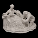 Estatueta em porcelana alemã branca representando casal em cena romântica, durante a leitura. Base recortada. No verso, marca da manufatura de Nymphenburg (Baviera). Fio de cabelo na lateral. 17 x 23 cm.