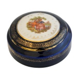 Caixa circular em porcelana francesa azul noturno, com detalhes em dourado e representação de cena galante ao centro da tampa. No fundo as inscrições Porcelaine, Made in France.  6 x 12 cm.