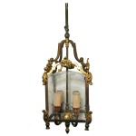 Elegante lustre francês para quatro luzes, de metal dourado. Estrutura com adornos estilizados. Laterais em vidro bisotê. 50 cm.