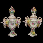 Par de ânforas em porcelana alemã policromada, decoradas com flores e pares de anjos sentados nas alças laterais. Bases recortadas. Nos versos, marcas da manufatura de Plaue. 11 cm. 