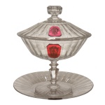 BACCARAT - BARÃO DE JUNDIAI - Compoteira com presentoir em cristal translucido. Tampa com pega sextavada e franchada. Decoração canelada, fuste sextavado e base redonda. Apresenta monograma entrelaçado sobre cristal cereja, no bojo e na tampa. França. Séc. XX.  20 x 17 cm (compoteira). 19 cm (presentoir).
