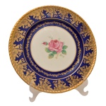 Prato em porcelana inglesa Paragon, com borda em ouro e azul cobalto, com arranjos florais ao centro sobre fundo branco. No verso as inscrições: Paragon Fine Bone China by Appointmente China Potters to Her Majestic Queen Elizabeth. Made in England. 27 cm.