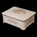 Caixa retangular em porcelana inglesa Paragon, com detalhes em alto relevo da própria porcelana e desenho de flores. Bordas da tampa e pés em dourado. 5 x 12,5 x 9,5 cm.