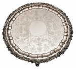 Salva em metal inglês batido, repuxado e cinzelado de forma circular, apresentando borda rebuscada com folhas de acanto guilhochadas. Reserva central lavrada a cinzel e três pés fitomórficos no estado. Inglaterra. Séc. XIX. 40 cm. Pertencente ao acervo do Dr. Renato de Magalhães Gouvêa.
