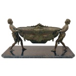 Escultura em bronze patinado representando floreira de formato oval, ornada por adornos estilizados e sustentada por figuras masculinas nas laterais. Base retangular. 7 x 52 x 23 cm. / 58 x 25 cm.
