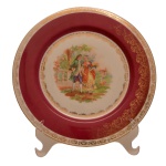 Prato de porcelana alemã Bavária. Borda com decoração em ouro e vermelha e centro com representação de cena galante. No fundo as inscrições: Made in Germany/U.S. Zone. 26 cm.