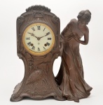 Relógio de mesa de estilo e época `Art Noveau`. Composto por maquinário da manufatura norte-americana de `Ansonia`, fixo a caixa em petit bronze fundido como pedestal, lavrado com atributos do movimento, seguido de figura de dama apoiada sobre sua face esquerda. França. C. 1905. 4 x 30 x 17 cm.