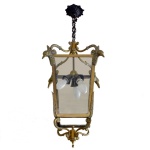 Luminária de teto para três lâmpadas, em latão dourado e formato de caixa. Figuras de beija flores, fundidos em bronze, destacam-se nos cantos superiores. Possui quatro lados em vidro, finalizados por volutas presas a cilindro decorativo. Canopla e corrente em bronze. 75 x 36 cm