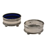 Par de saleiros em prata inglesa, decorados com frisos geométricos fenestrados; um deles é guarnecido com recipiente em cristal azul. Apoiados em quatro pés, formato bolacha. Contrastes da cidade de Birmingham de 1918 e da manufatura Gorham Manufacturing Co. Falta 1 recipiente. 4 cm. 114 gramas.