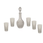 Conjunto de licoreiro em cristal com quatro copos baixos. Garrafa de formato piriforme com longo gargalo e tampa moldada em pinha. Decoração lapidada com reservas geométricos e adornos estilizados. 34 cm (licoreiro), 13,5 cm (copos).