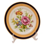 Prato em porcelana francesa Limoges com borda em ouro e azul cobalto. Arranjos florais ao centro sobre fundo branco. No fundo as inscrições: Limoges, France. 25 cm.