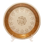 Medalhão em porcelana alemã. Borda com friso branco e larga faixa em ouro e decoração ao centro de arabescos sobre fundo branco. No fundo as inscrições: Winterling Bavaria, Germany e etiqueta J. de Backer, Bevere. 29 cm.