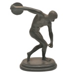 Escultura em bronze patinado representando `O Discóbolo`, símbolo da Educação Física, inspirado na famosa escultura atribuída a Myron, renomado escultor grego do séc. V a.C. Base ovalada. 18 x 12 cm.