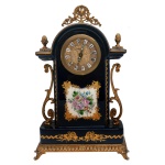Relógio de mesa de porcelana francesa A.C.F. décor bleu Sèvres, fait à la main, em azul noturno e guarnição em bronze, com dourado e flores. Caixa retangular com topo arqueado e mostrador com números romanos. Base retangular seguindo a mesma decoração. Máquina do relógio Made in Germany. Mecanismo movido à corda. 25 x 15,5 x 7 cm.