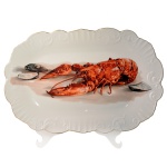 Travessa de porcelana portuguesa apresentando superfície branca tendo ao centro uma lagosta. Relevos nas extremidades e bordas em filete dourado. Marcas no verso com as inscrições "Decor Eva Portugal". Séc. XX. 42 x 28 cm.