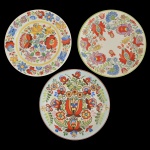 Conjunto de três pratos de porcelana. Apresenta centro com decoração floral predominando as cores amarela, azul e vermelha. No verso as inscrições: Hungarian Polk Art Hand Painted, Gal. 26 cm. 