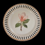 Prato de porcelana europeia. Apresenta borda fenestrada e centro com decoração floral. 25 cm. 