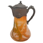 "Claret Jug", de formato piriforme, em pasta de vidro decorado com folhagens em tons de amarelo e verde. Parte superior em metal prateado com bico, tampa e alça moldados. Apresenta depósito interno para gelo. No verso, marca francesa. 11 x 6.5 cm.