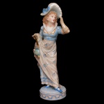 Estatueta em porcelana francesa representando dama com chapéu. Base circular. No verso, marca da manufatura Gille Jeune - Vion et Baury, Paris (1836-1889). 17 x 5 cm.