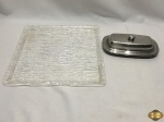 Lote composto de manteigueira em aço inox e bandeja em acrílico. Medindo a bandeja 30,5cm x 30,5cm.