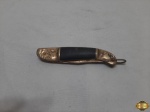 Canivete Tailnades em metal dourado trabalhado com relevos e pega em resina preta. Medindo 14cm de comprimento aberto.