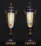 Par de ânforas de porcelana estilo Sévres, fundo azul noturno com reservas frente e verso,decorados com esmaltes policrômicos; montagem em bronze. 49 cm de altura. (1 tampa restaurada).