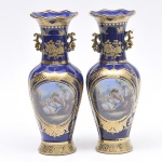 Par de Ânforas estilo Luiz XV em porcelana azul cobalto ao gosto de sevres decoradas com cena galante em fina policromia e guarnição floral dourada. Med: 30cm de altura